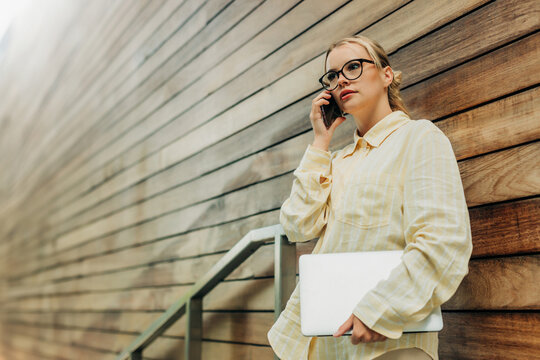 Female entrepreneur talking on smartphone while holding laptop outdoors