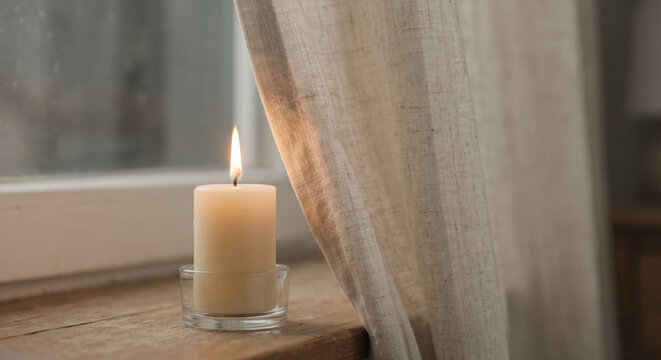 Lit candle burning dangerously close to linen curtain near window fire hazard and home safety concept