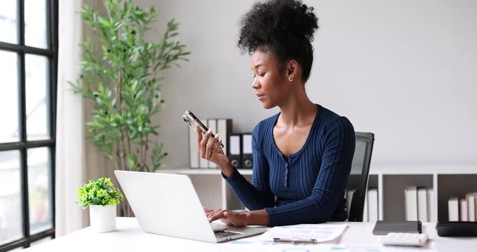 African american businesswoman working with laptop and smartphone in modern office, managing business, communicating, networking, and staying productive indoors