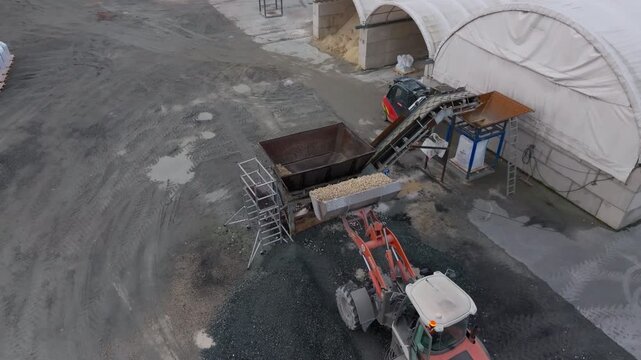 Aerial View, loader feeding aggregate into a hopper at a quarry processing plant, showing conveyor machinery, raw material handling, construction, and mining industry themes