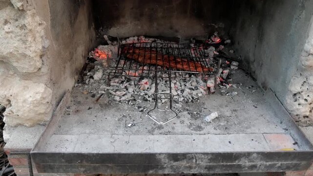 Meat grilling over hot coals in a stone barbecue with metal grate outdoors