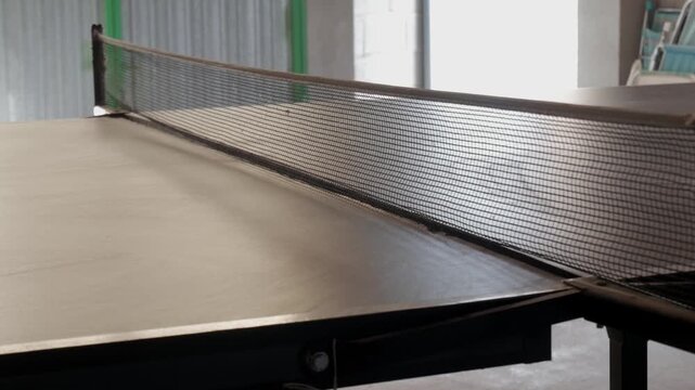 Orange ping pong ball bounces over table tennis net in an indoor recreation space