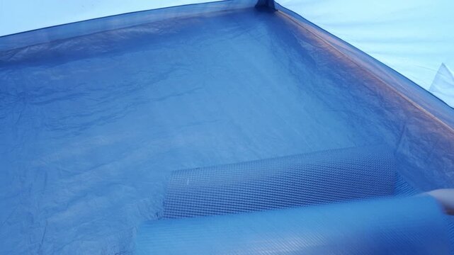 Person unrolling a sleeping pad on tent floor for campsite setup or preparation