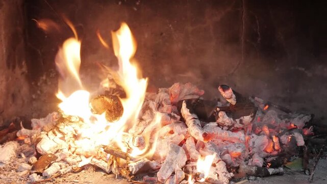 Hand stirs hot embers and ashes in a fireplace, spreading glowing coals for cooking