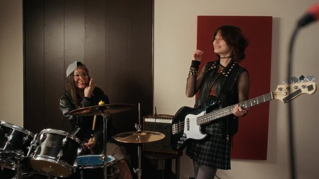 Caucasian teenage girls playing drums and bass guitar, laughing and fist bumping during music rehearsal in studio. Footage is ideal for youth lifestyle and creative hobby commercials