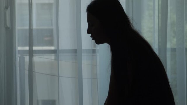 Expat woman sitting alone in temporary apartment feeling emotionally exhausted from constant relocation, homesickness and lack of belonging, close up silhouette