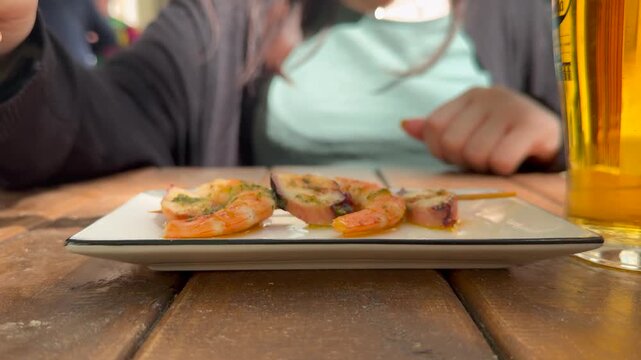 Closeup view of the hands of a caucasian young woman eating traditional spanish seafood tapas and beer sitting outdoor in a. terrace.