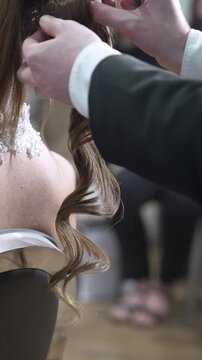 A groom assists his bride with her wedding dress in a lively room filled with guests. They share a special moment before the ceremony begins, showcasing their love and connection.