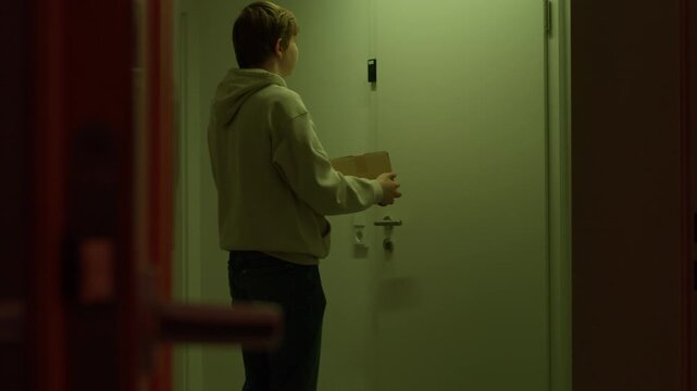 Courier walks away after leaving a parcel at an apartment door following confirming delivery via intercom device, useful for logistics, ecommerce, customer service and security themes