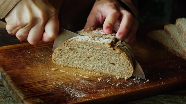 Hands slicing freshly baked loaf of brown gluten free bread on cutting board
