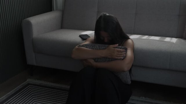 Sadness and pain after breakup. Young woman hugging pillow on floor feeling lonely and heartbroken after losing her