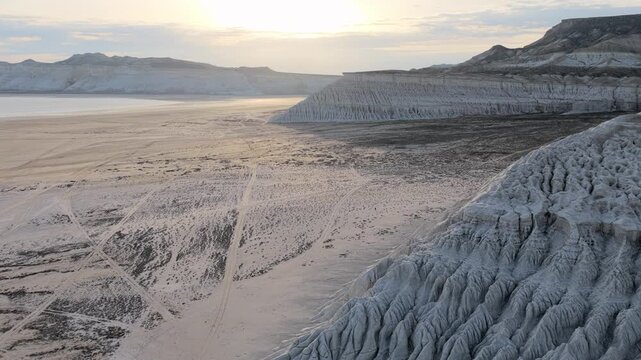Aerial view of the white salt flats and eroded limestone cliffs of Tuzbair under a soft golden sky in Mangystau District, Mangystau Region, Kazakhstan.