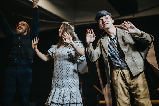 Young actors bow on stage after finishing a scene. Theatre cast acknowledges applause during a curtain call