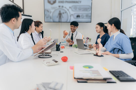 Medical teamwork concept with Asian healthcare professionals discussing internal organ models and patient analysis charts on digital screen during an office meeting.