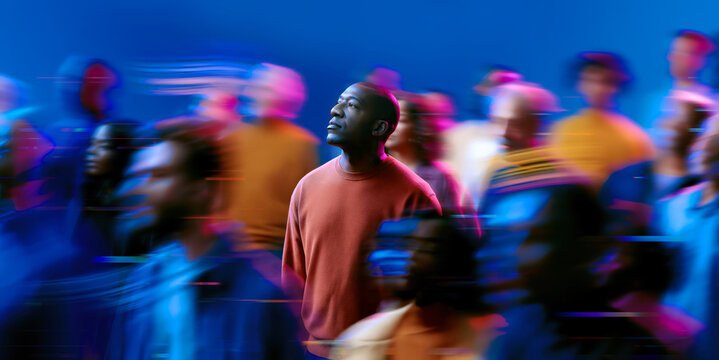 Thoughtful African American man standing still as vibrant neon crowd rushes past in blue and magenta