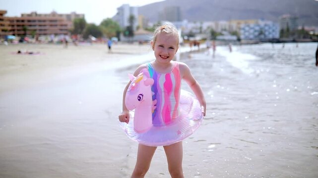 Little girl playing in shallow sea water with an inflatable unicorn swim ring in Los Cristianos, Tenerife, Canary Islands, Spain