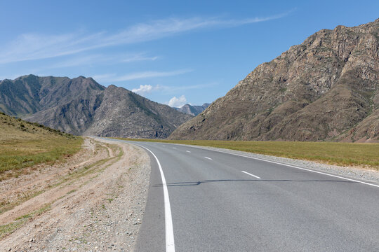 Empty asphalt road of the Chuysky Trakt winding through rugged Altai Mountains under blue sky, scenic travel route in Altai Republic, Russia