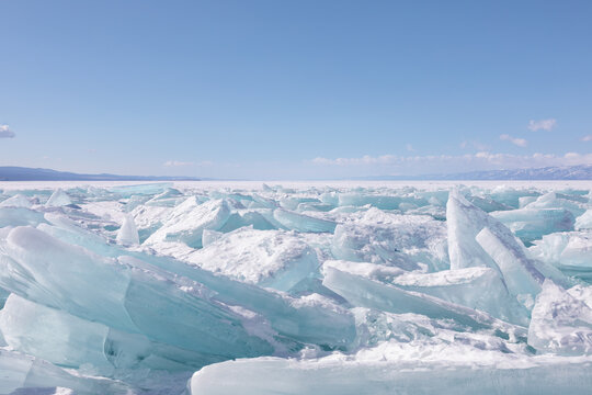 Wide winter landscape of frozen Lake Baikal with turquoise ice blocks and pressure ridges on the shoreline, clear blue sky and distant mountains, Russia