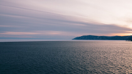 Fototapeta premium Wide panoramic landscape of Lake Baikal at sunset with calm rippled water, pastel sky and distant rocky shoreline near Listvyanka, Irkutsk Oblast, Russia
