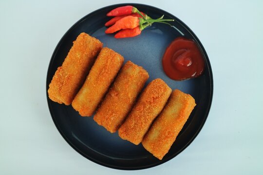 This is risoles (or risol), a popular Indonesian snack with a rough, crispy outer crust and a soft, sliced ​​chicken filling. It's served on a black plate with chili sauce and red chili.