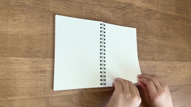 Child Hands Turning One Page of a Small Notebook from Right to Left on a Wooden Table, 4K Silent Video