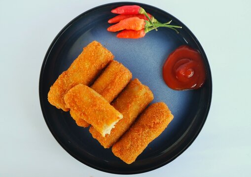 This is risoles (or risol), a popular Indonesian snack with a rough, crispy outer crust and a soft, sliced ​​chicken filling. It's served on a black plate with chili sauce and red chili.