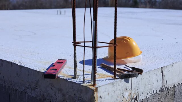 Construction tools and helmet on a cement foundation with iron rebar.