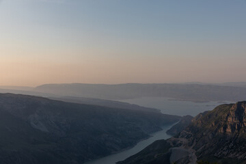 Fototapeta premium Wide panoramic landscape of Sulak Canyon with winding river and layered mountain ridges at sunrise, atmospheric haze and calm sky in Dagestan, Russia