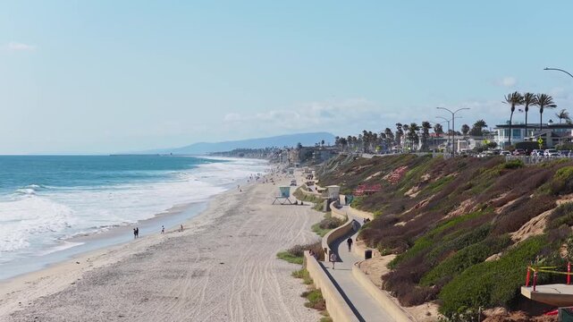 People walk along Carlsbad State Beach on a sunny day in California with Pacific Ocean and coastal bluffs creating scenic California coastline travel destination