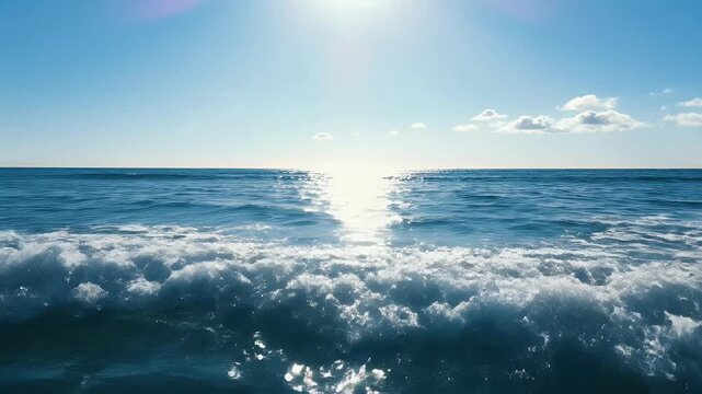 Bright sun glints off gentle waves under a clear blue sky with fluffy clouds