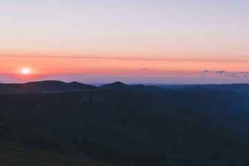 Obraz premium Wide landscape view of sunrise over Bermamyt Plateau, Karachay-Cherkess Republic, Russia, with dark mountain silhouettes, soft clouds, and colorful dawn sky