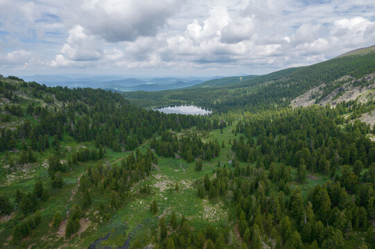 Wide panoramic view of Karakol Lakes surrounded by taiga forest and green mountain slopes under dramatic clouds in Altai Republic, Russia, summer wilderness travel scene