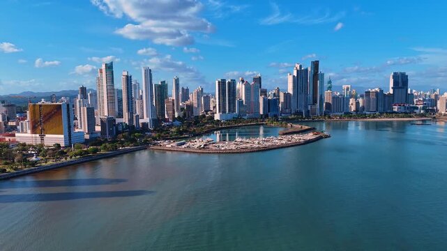 Waterfront skyline of Panama City with marina and bay reflections. Wide angle showing skyscrapers, docked yachts and calm water under scattered clouds.