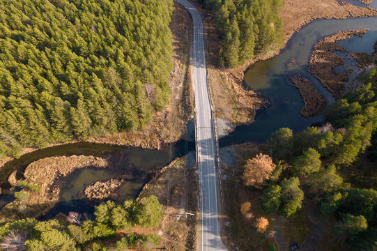 Top down aerial view of a paved road bridge crossing a winding river and wetlands, surrounded by mixed forest in Sverdlovsk Oblast, Russia, autumn landscape
