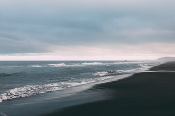 Fototapeta premium Moody ocean waves roll onto the black volcanic sand of Khalaktyrsky Beach near Petropavlovsk-Kamchatsky, Kamchatka Krai, Russia under overcast skies