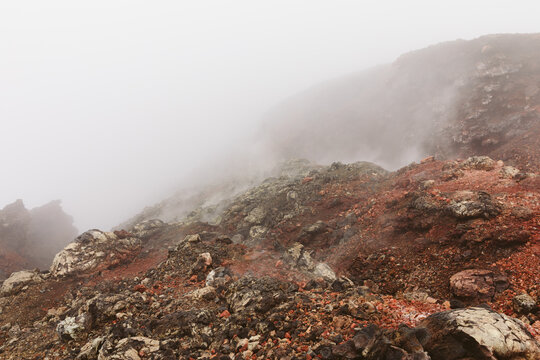 Mist and steam drift over rugged red volcanic rocks in the Northern Breakthrough area of Tolbachinsky Dol, Kamchatka Krai, Russia, creating an eerie barren landscape