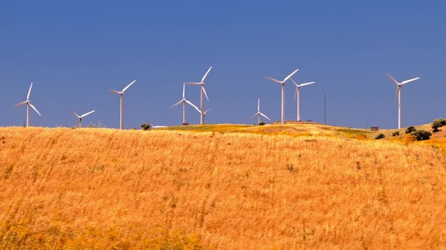 Cinematic drone footage of a large wind farm with turbines generating clean renewable electricity across a rural landscape. Sustainable energy infrastructure supporting decarbonization and climate goa
