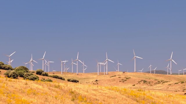 Cinematic drone footage of a large wind farm with turbines generating clean renewable electricity across a rural landscape. Sustainable energy infrastructure supporting decarbonization and climate goa