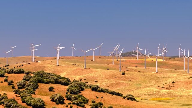 Cinematic drone footage of a large wind farm with turbines generating clean renewable electricity across a rural landscape. Sustainable energy infrastructure supporting decarbonization and climate goa