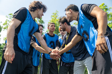 Naklejka premium Diverse group of young soccer players stacking hands with coach before football match outdoor. Multiethnic athletes huddle together showing team unity at green field
