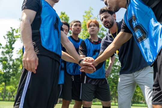Diverse group of young soccer players stacking hands with coach before football match outdoor. Multiethnic athletes huddle together showing team unity at green field