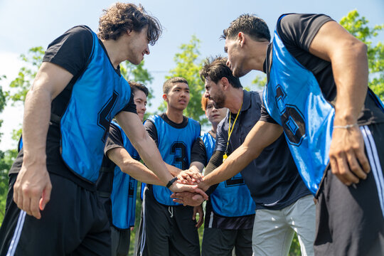 Diverse group of young soccer players stacking hands with coach before football match outdoor. Multiethnic athletes huddle together showing team unity at green field