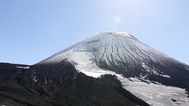 Wide landscape view of Avachinsky Volcano with snow and dark volcanic slopes under a clear blue sky in Kamchatka Krai, Russia, a remote volcanic travel destination