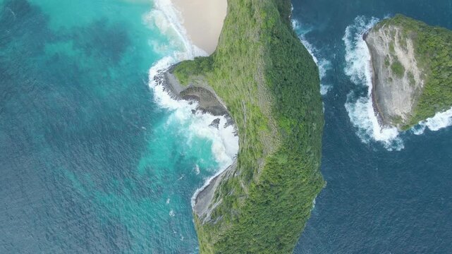 Cinematic birds eye view of the iconic TRex shaped cliff at Kelingking Beach, Nusa Penida, Bali. Featuring turquoise ocean waves crashing against white sand and lush green limestone rocks.