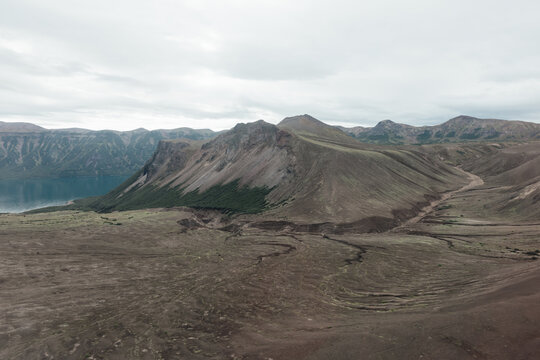 Wide view of the Ksudach volcano caldera with crater lake, barren lava fields and layered ridges under cloudy sky in Kamchatka Krai, Russia