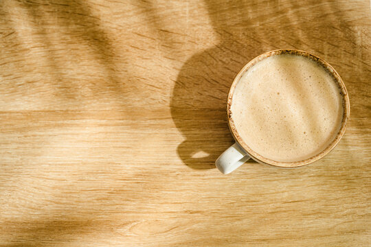 Top view of coffee cup on wooden desk with copy space and natural sunlight