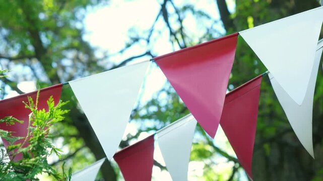 Red and white pennant flags strung outdoors with blurred green trees