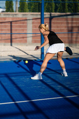 Obraz premium Woman playing padel on blue court hitting ball