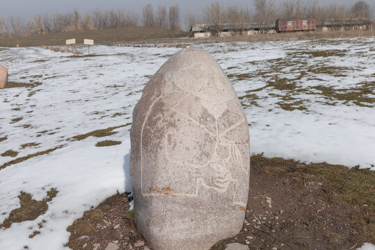 Tokmok, Kyrgyzstan - February 27, 2025: Weathered carved stone balbal standing in a snowy field at the Burana Tower archaeological complex near Tokmok, Chuy Region, Central Asia travel heritage