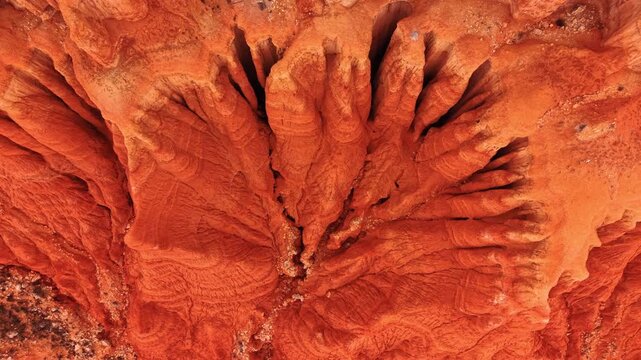 Top down view of fan shaped erosion ridges in red earth, Spain. Symmetrical clay fingers radiate from central gully in warm orange tones.